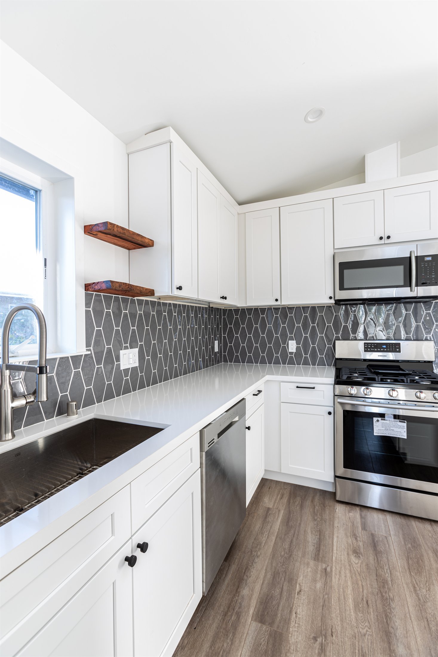 Completed ADU kitchen with white cabinetry, gray tile backsplash, and stainless steel appliances